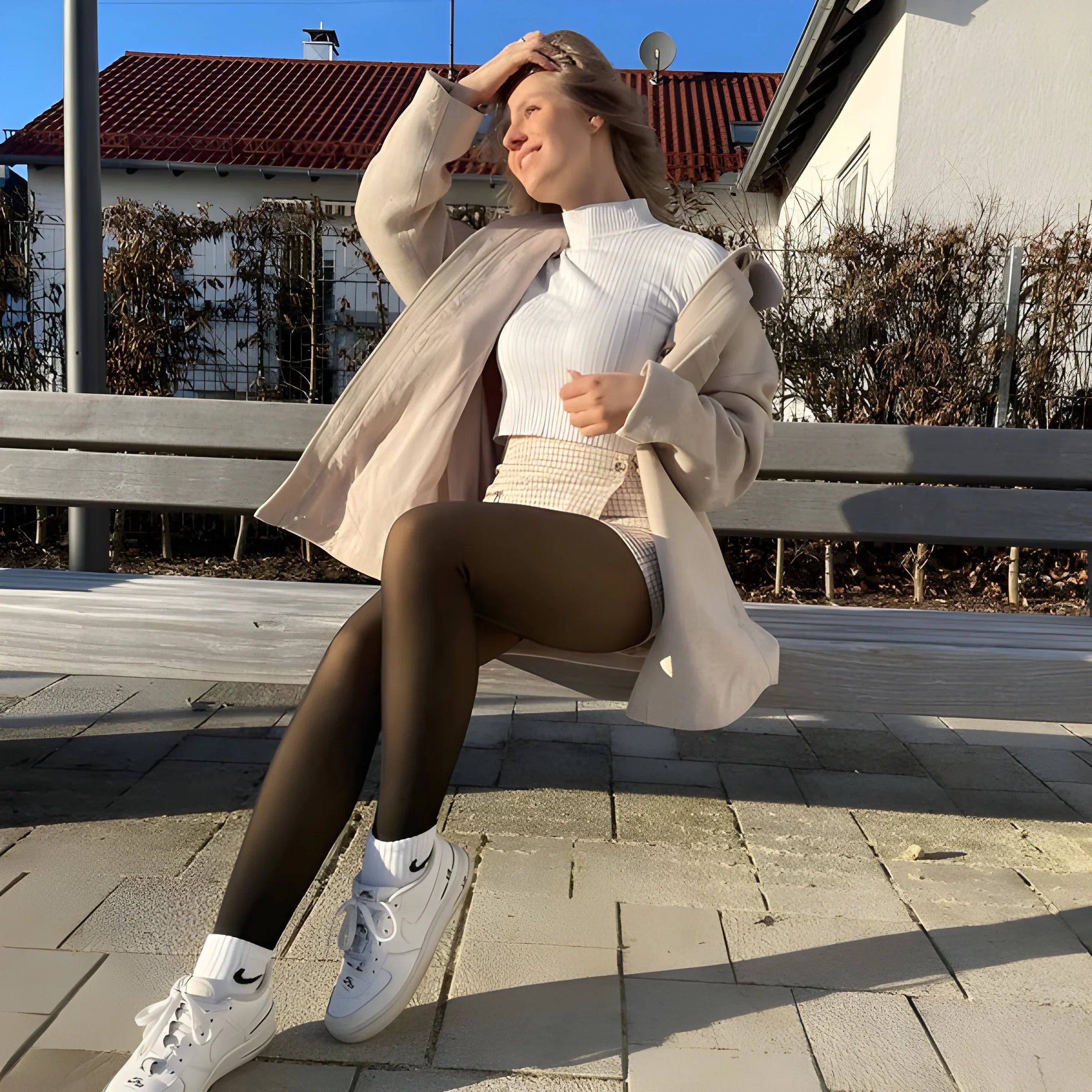 Woman wearing Formivelle fleece-lined tights, white jacket and sneakers, sitting on bench outdoors